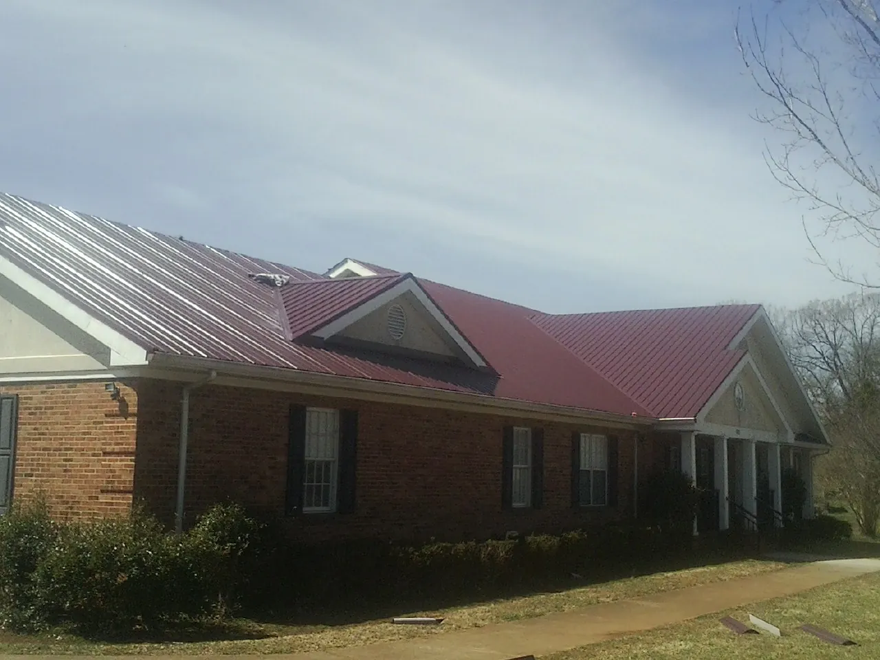 Red metal roof with gabled entries on a long brick building, from a Hail Damage Roof Repair job in Pleasant Plains