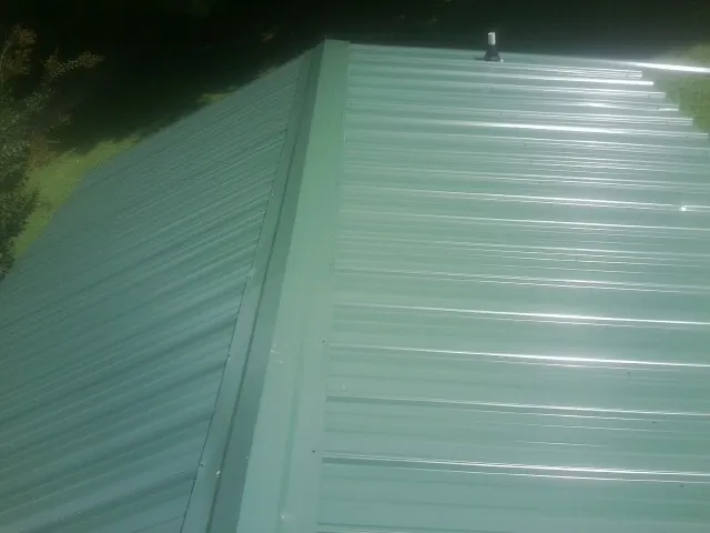 New green metal panels meeting at the ridge of a roof — Flat Roof Repair work by our crew in Pleasant Plains