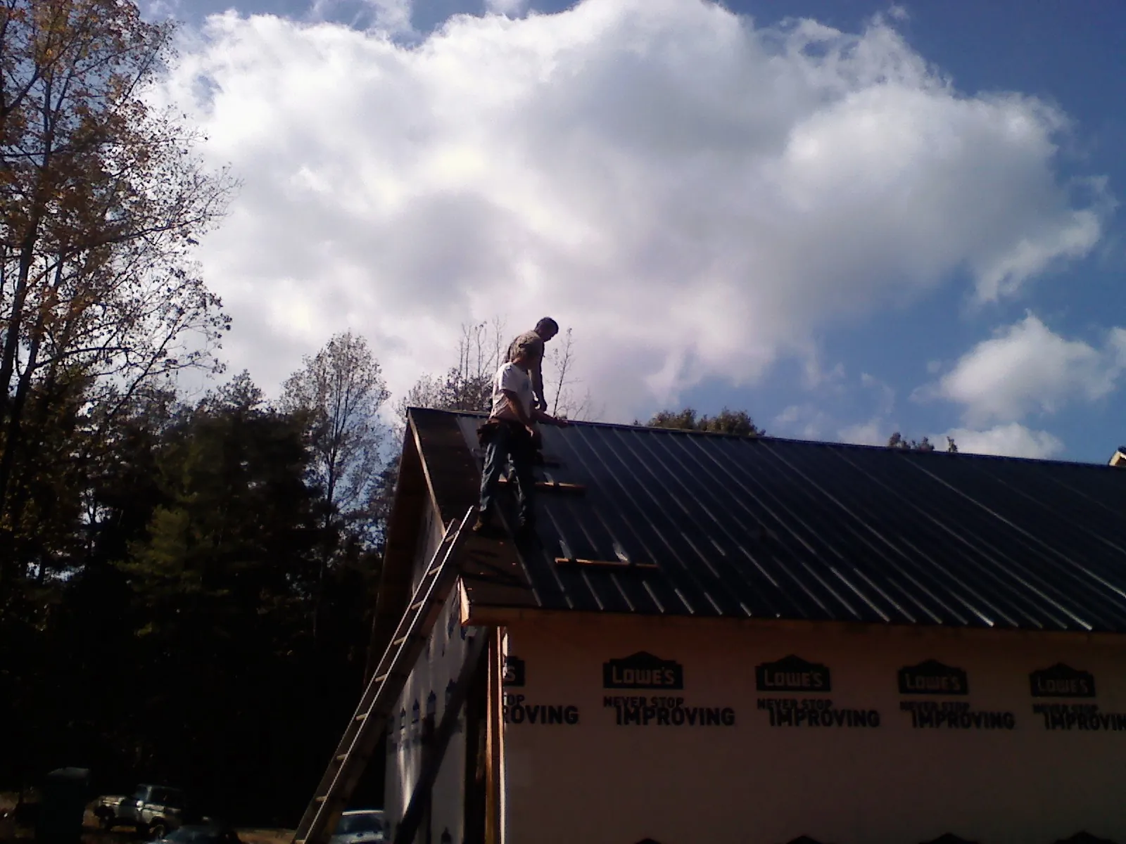 Roofer fastening dark metal panels high against a cloudy sky, from a Roof Inspection job in Pleasant Plains
