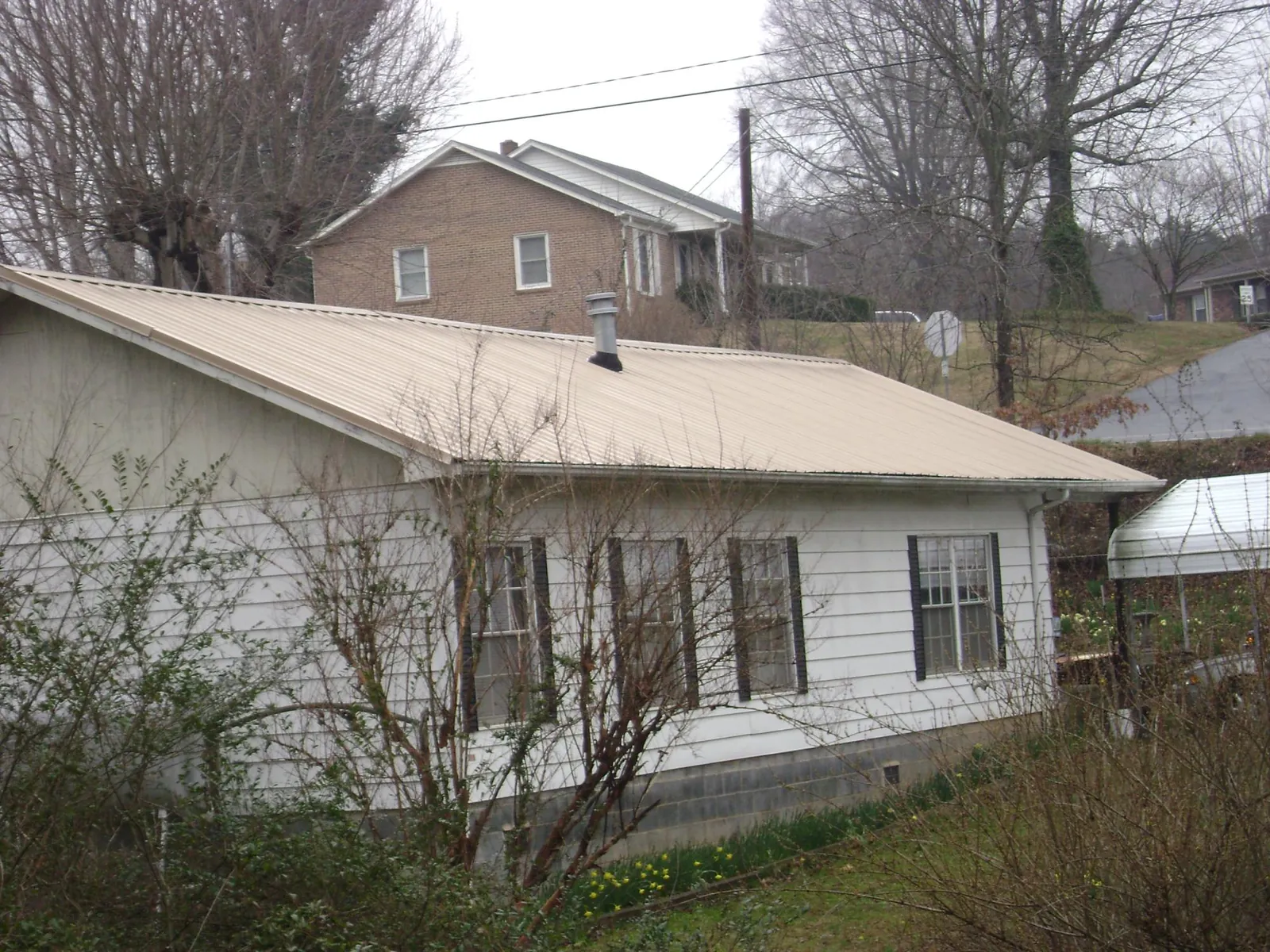 Tan metal roof on a white sided house set into a hillside — Commercial Roofing by Roofing Brothers in Pleasant Plains