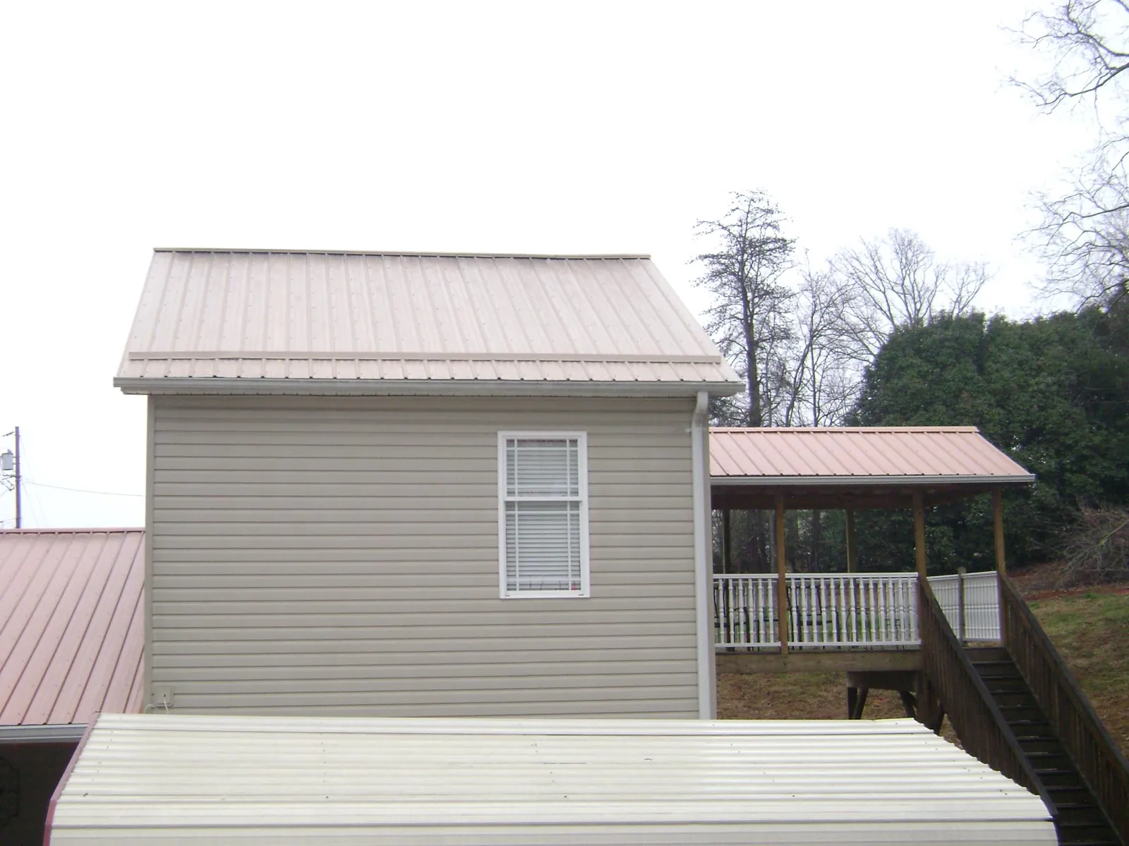 Tan metal roofs on a two story addition and attached porch, from a Roof Replacement job in Pleasant Plains
